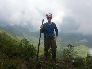 Michael Altfield holding a bamboo trekking pole, surrounded by clouds and lush green, rolling hills